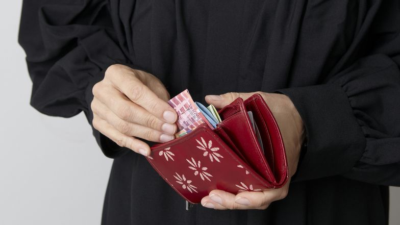 Jemand nimnt Noten aus einem Portemonnaie.