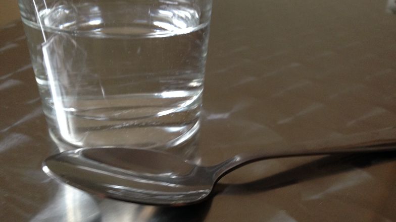 Ein Glas mit einer Flüssigkeit und ein Löffel.