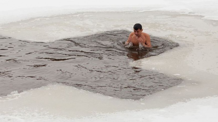 Mann badet in Eisloch, das Form eines Kreuzes hat