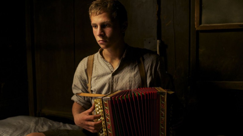 Das Bild zeigt eine Szene aus dem Film «Der Verdingbub». Ein Junge spielt in einem Zimmer Ziehharmonika und blickt dabei traurig in den Raum.