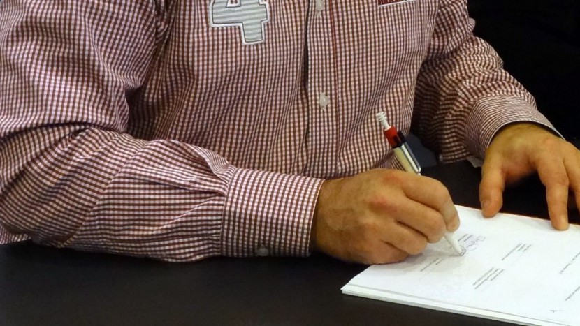 Das Bild zeigt einen Mann beim Unterzeichnen eines Vertrages